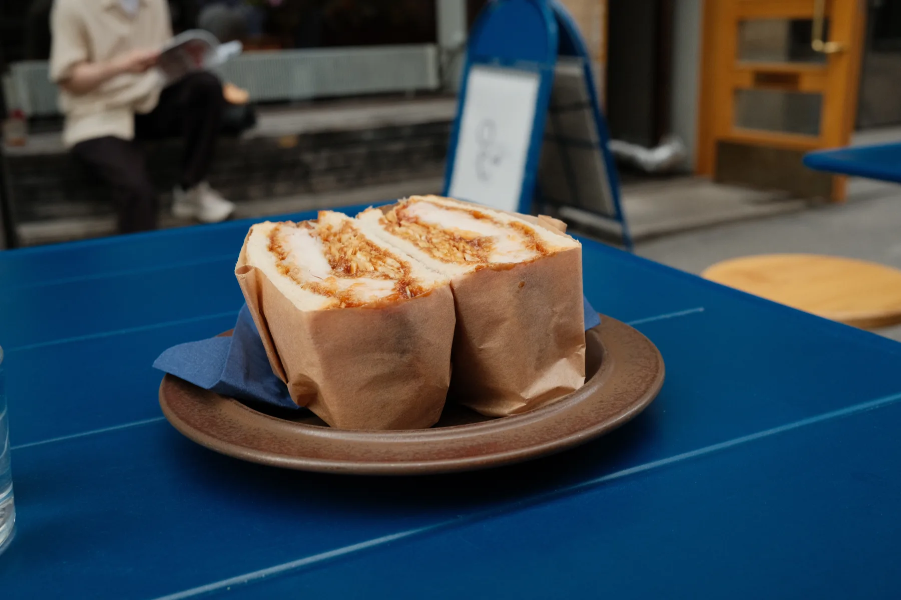 A katsu sando cut in half on a plate on Café Tampopo's blue terrace table