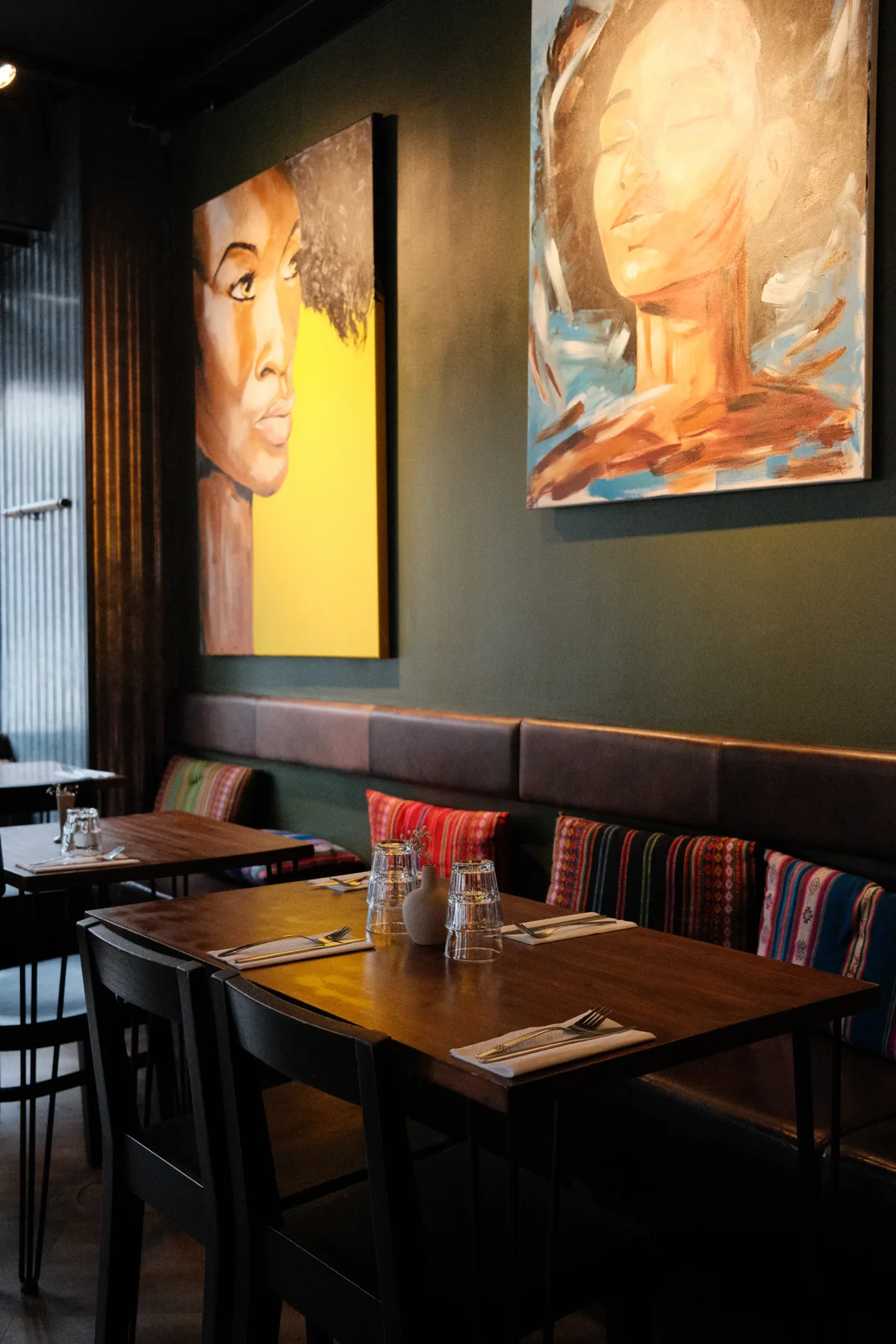 Set tables, colorful woven cushions, and portrait paintings inside Tinku's green dining room