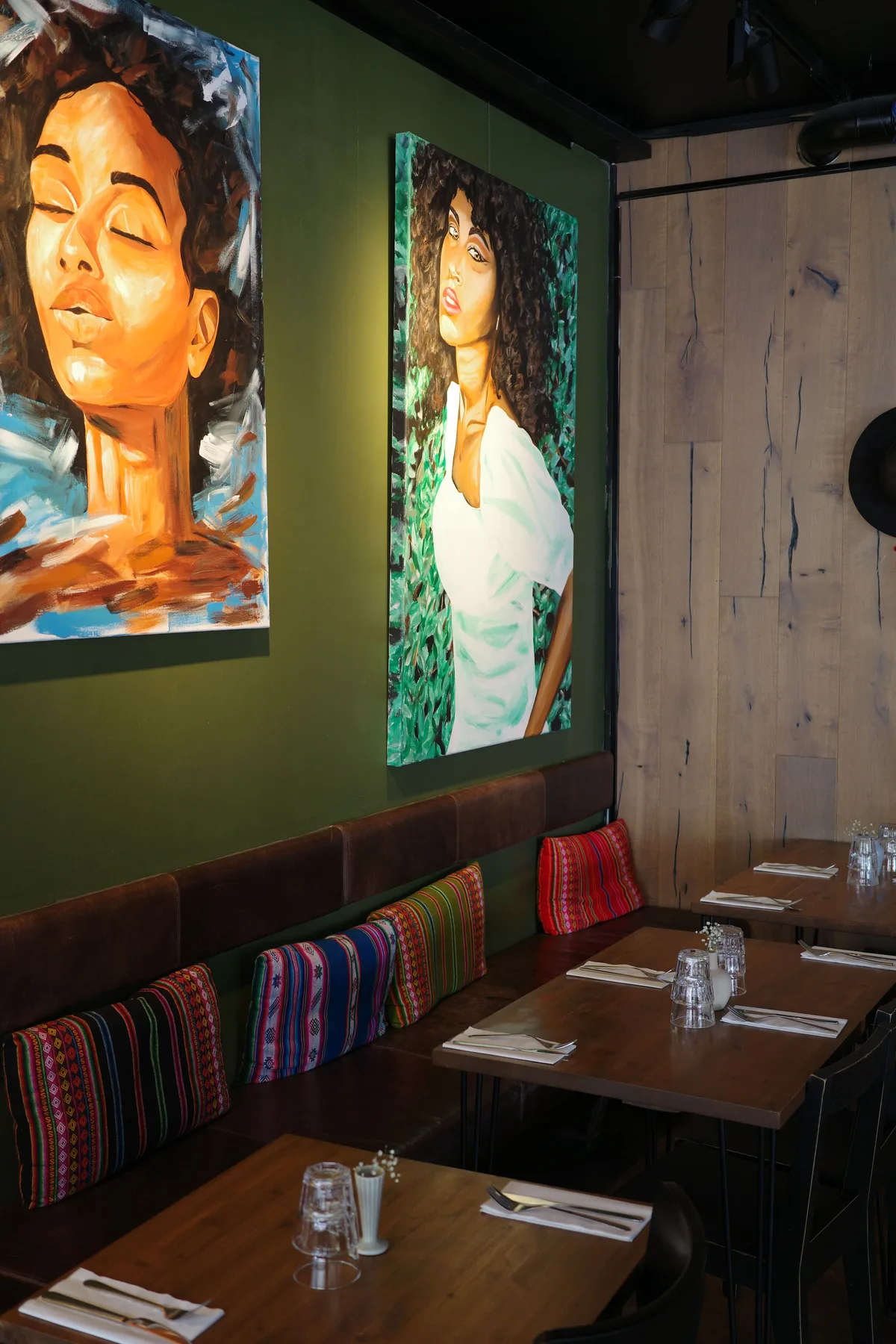 Tinku's green dining room with portrait paintings, woven cushions, and set tables